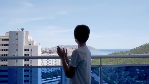 A fiú tapsol, integet, üdvözöl a szomszédokkal. Tapsolás az erkélyről az orvosok, nővérek, kórházi dolgozók támogatására Spanyolországban a Coronavirus világjárvány idején karantén - Felvétel, videó