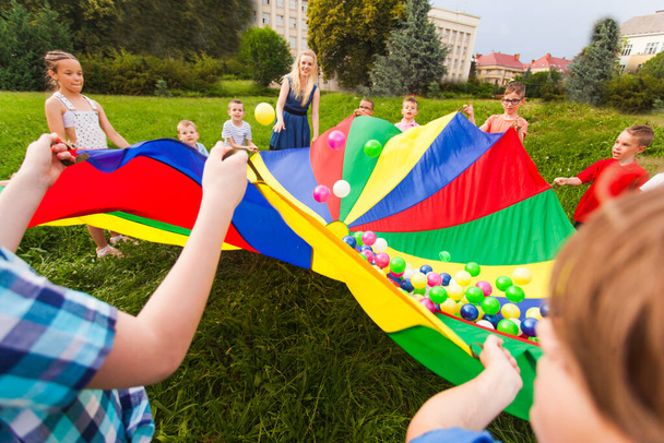 Kids holding rainbow parachute with colorful balls on it - Foto, afbeelding