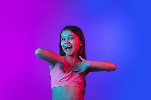 Little caucasian girls portrait isolated on gradient pink-blue background in neon light. - Foto, imagen