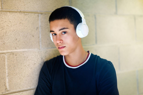 Egy tinédzser fejhallgatót visel, és komoly arckifejezéssel néz a kamerába, miközben neki hajol egy csempézett falnak fénymásoló felülettel. - Fotó, kép