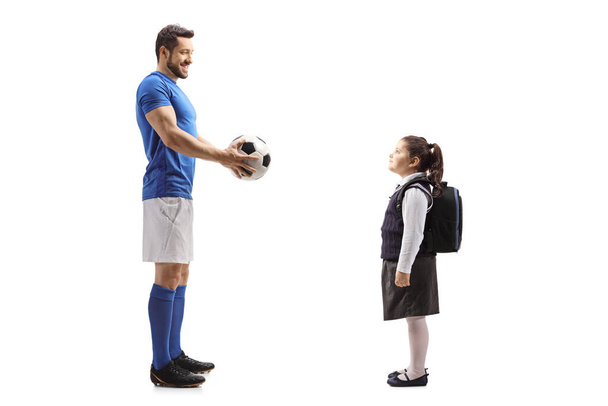 Full length profile shot of a footballer giving a soccer ball to a schoolgirl isolated on white background - Foto, Imagem