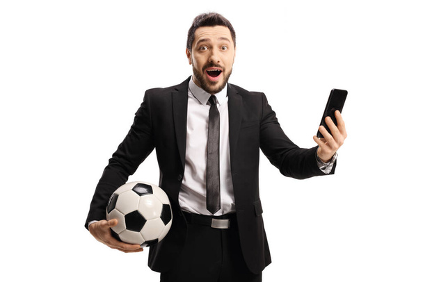 Excited man in a suit holding a soccer ball and a mobile phone isolated on white background - Φωτογραφία, εικόνα
