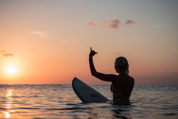 Portrait from the water of surfer girl with beautiful body on surfboard in the ocean at colourful sunset time in Bali - Photo, Image