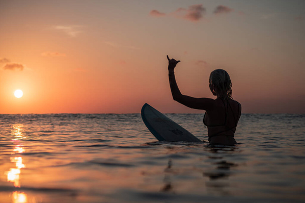 Portrait from the water of surfer girl with beautiful body on surfboard in the ocean at colourful sunset time in Bali - Photo, image