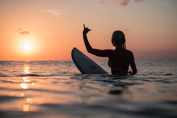 Portrait from the water of surfer girl with beautiful body on surfboard in the ocean at colourful sunset time in Bali - Fotó, kép