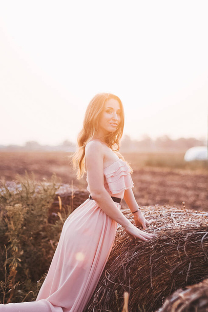Beautiful romantic model girl outdoors dressed in tende long dress in the field in sunset light. Wind blowing long hair. Glow Sun, Sunshine. Backlit. Toned in warm colors. - Photo, image