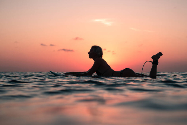 Portrait from the water of surfer girl with beautiful body on surfboard in the ocean at colourful sunset time in Bali - Фото, зображення