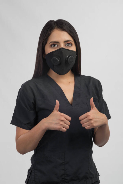 Latino-Ärztin optimistisch mit ihrer Biosicherheitsmaske und ihrem blauen medizinischen Anzug  - Foto, Bild