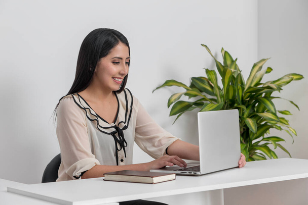 Latin bir kadın iş yerinde laptopuyla gülümsüyor.  - Fotoğraf, Görsel