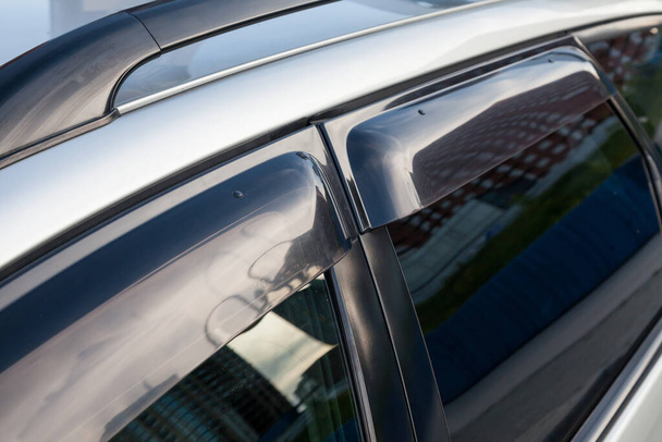 Close-up van de zijruiten van een auto sedan met plastic verduisterde pads die beschermen tegen wind en regen wanneer het raam open is. Elementen van het licht afstemmen van een grijze sedan. - Foto, afbeelding