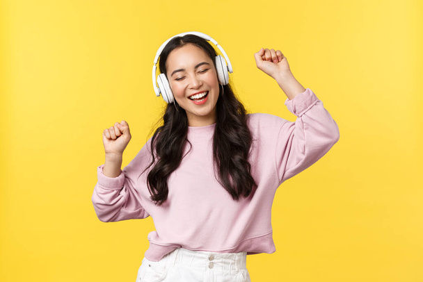 People emotions, lifestyle leisure and beauty concept. Joyful pretty asian woman in wireless headphones listening music, dancing excited with closed eyes and happy smile, listen favorite song - Foto, Imagen