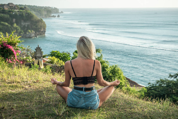 Portrait of young blonde woman meditates on the cliff with ocean view, waves, surf spot in Bali - Foto, Imagem