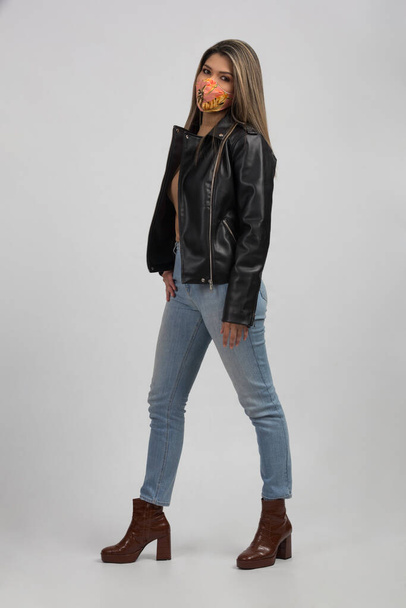 latino model woman wearing a tropical style face mask with a casual outfit jeans and black leather jacket   - Photo, Image