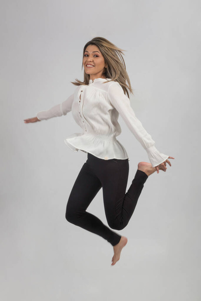 mujer joven saltando en un fondo gris, sonrisa - Foto, afbeelding