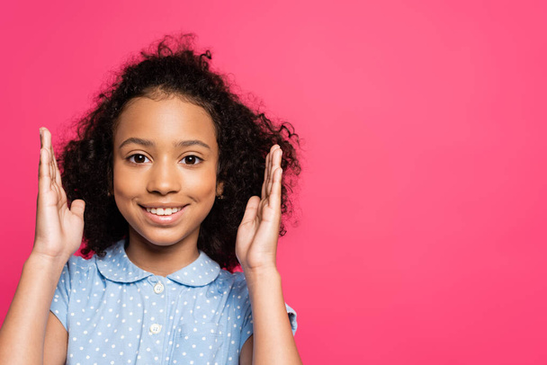 smiling cute curly african american kid with hands near face isolated on pink - Фото, зображення
