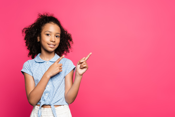 smiling cute curly african american kid pointing with  fingers aside isolated on pink - Photo, image