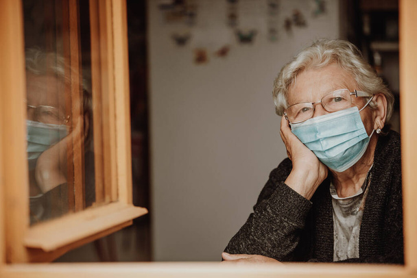 Portrait of lovely senior woman or grandmother, pensioner watching out from the window during pandemic covid-2019 - Foto, Bild