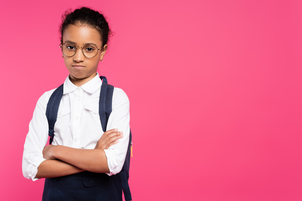 ofendida colegiala afroamericana en gafas con mochila y brazos cruzados aislados en rosa
 - Foto, Imagen