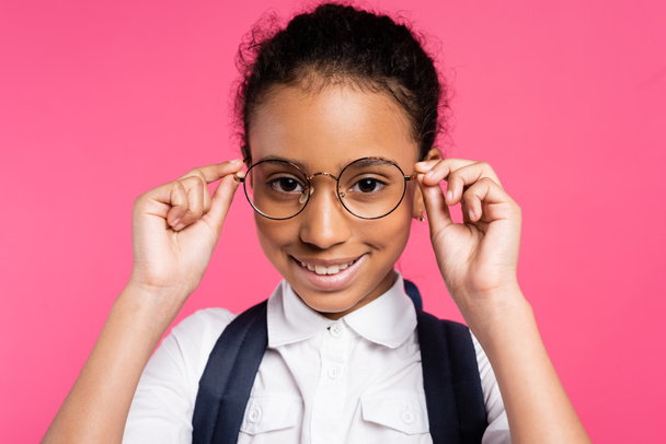 glimlachen Afrikaans amerikaans schoolmeisje aanpassen bril geïsoleerd op roze - Foto, afbeelding