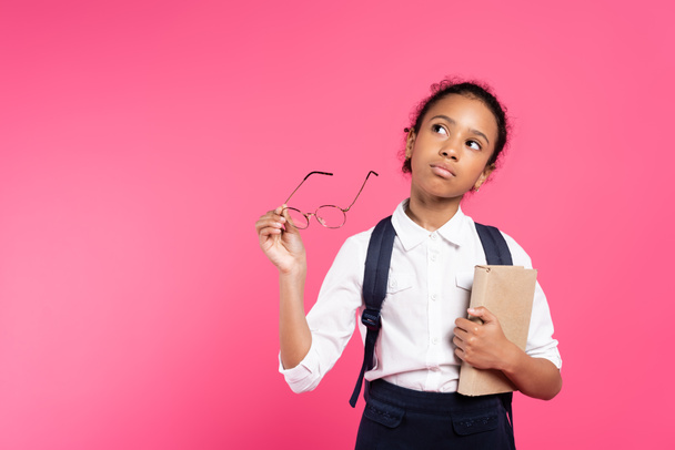 pensive african american schoolgirl with book and glasses isolated on pink - Photo, Image