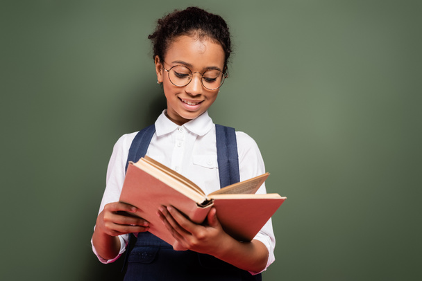 sonriente afroamericano colegiala lectura libro cerca vacío verde pizarra
 - Foto, Imagen