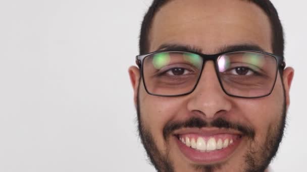 Retrato de cerca de un joven árabe de pie sobre un fondo blanco, sonriendo, mirando a la cámara
. - Imágenes, Vídeo
