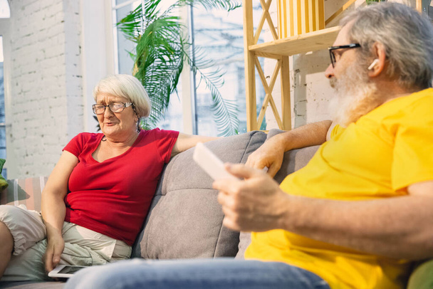 Couple of seniors spending time together being quarantined - caucasians mature and retired man and woman using modern gadgets, talking, drinking tea - 写真・画像