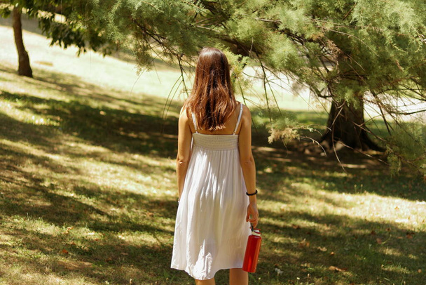 Chica en vestido blanco en el parque con cantina de agua roja
 - Foto, imagen
