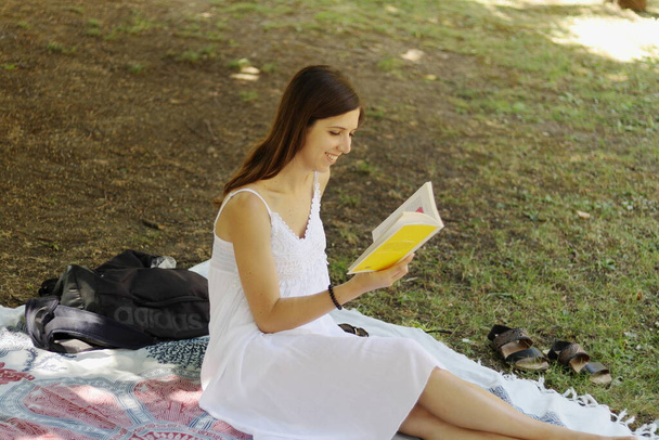 Meisje met witte jurk zittend op een boom met een boek - Foto, afbeelding