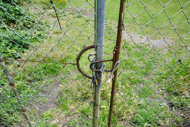 Großer Zaun mit Maschendraht und Stacheldraht, Kette und Vorhängeschloss. Grünland, Wiese, Baustelle - Foto, Bild