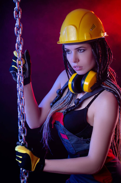 una chica de la construcción con un sombrero duro y un mono con una larga cadena en las manos - Foto, imagen