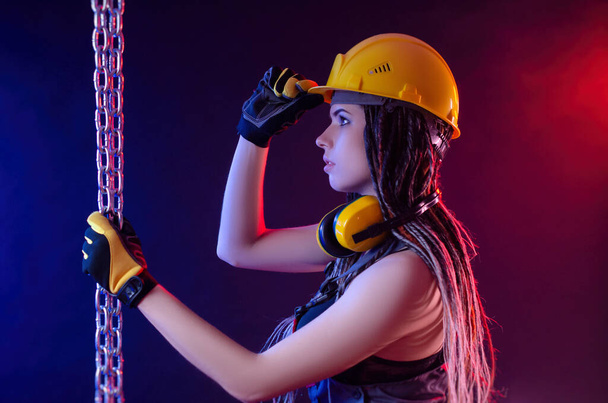 a construction girl in a hard hat and overalls with a long chain in her hands - Photo, image
