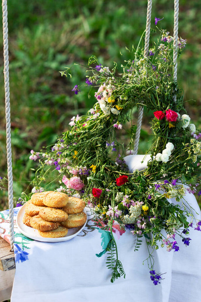 Shortbread koekjes met blauwe kaas en sesamzaad en een krans van wilde bloemen op een schommel. Rustieke stijl. - Foto, afbeelding