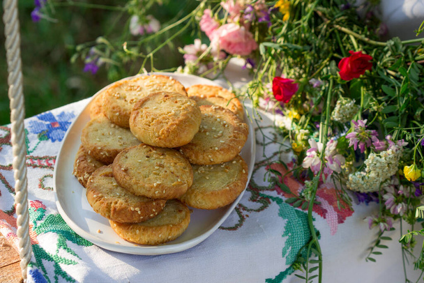 Galletas de pan corto con queso azul y semillas de sésamo y una corona de flores silvestres en un columpio. Estilo rústico
. - Foto, Imagen