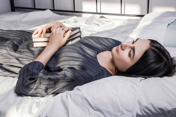 Mujer acostada en la cama y sosteniendo un montón de libros en sus manos, enfoque selectivo
 - Foto, imagen