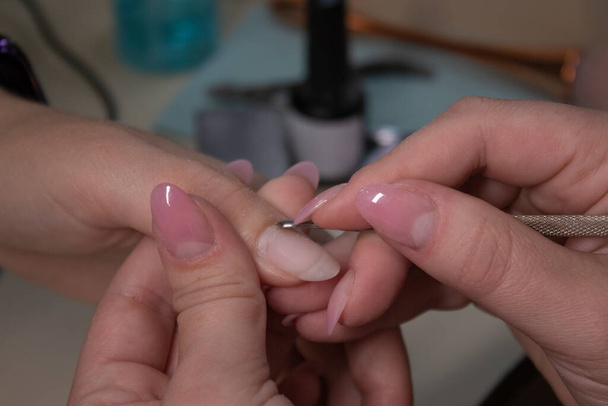 the process of doing manicure. Closeup of hands of professional manicurist, removing cuticle in salon. Concept of doing manicure and fingernails cleaning. beauty concept. Gel polish, shellac. - Photo, Image