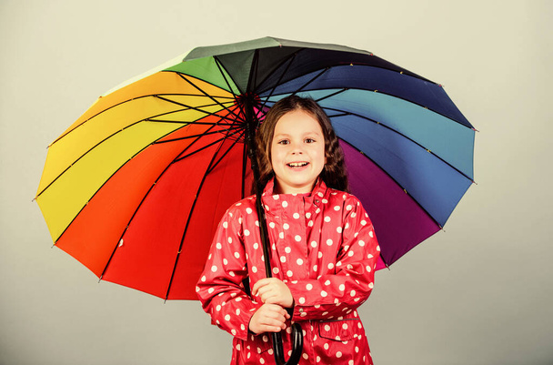 Kid girl happy hold colorful rainbow umbrella. Rainy weather with proper garments. Rainy day fun. Happy walk under umbrella. There is rainbow always after the rain. Enjoy rain concept. Fall season - 写真・画像