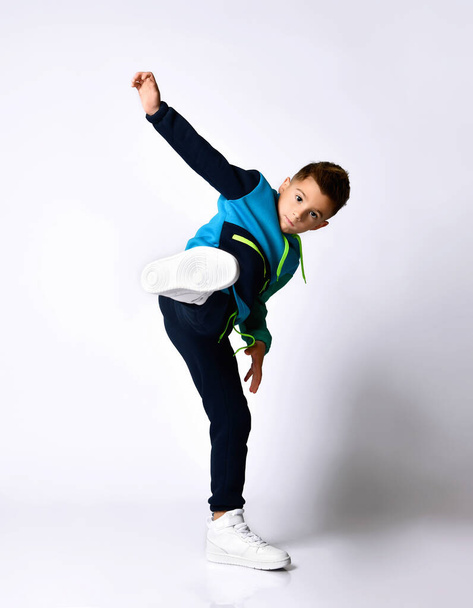 Little male in colorful tracksuit, sneakers. He performing a kick by his leg, posing isolated on white background - Valokuva, kuva
