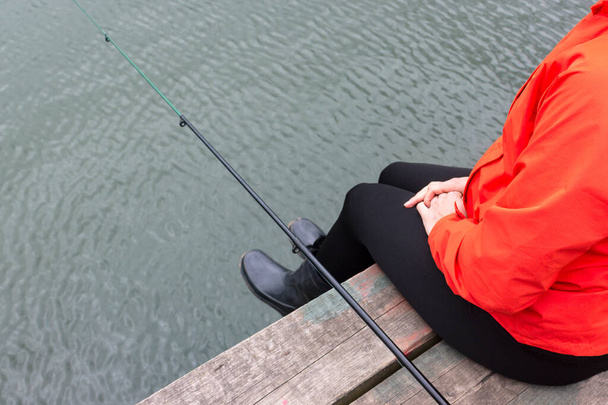 młoda piękna rybak dziewczyna połowów z prętem w dużym stawie. Ta kobieta nosi pomarańczową kurtkę. Aktywny sport i relaks dla kobiet - Zdjęcie, obraz