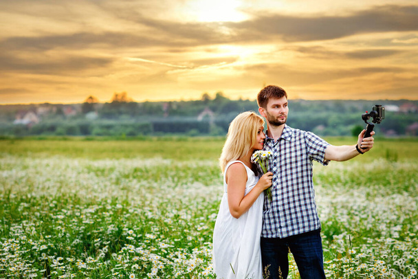 A man and a woman film themselves using a Steadicam in a chamomile field at sunset - Photo, Image