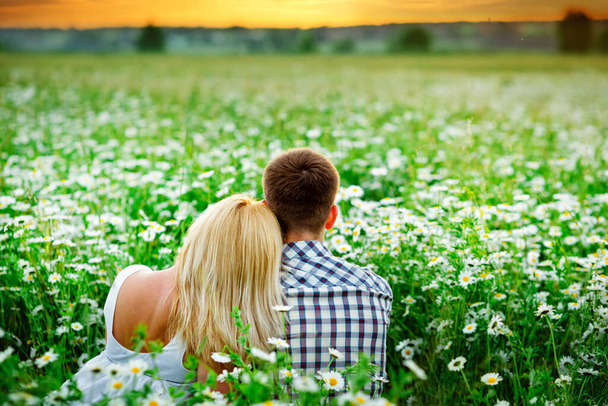 um jovem casal abraça ao ar livre em um campo de margaridas ao pôr do sol. Voltem para a câmara. Eles vêem o pôr-do-sol
. - Foto, Imagem