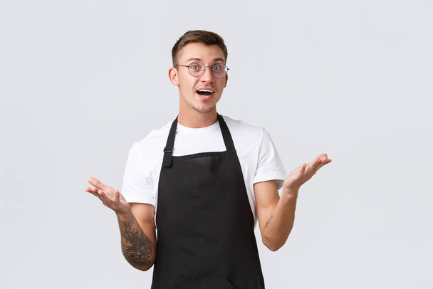 Small retail business owners, cafe and restaurant employees concept. Handsome friendly waiter, barista welcoming clients near counter, raising hands up and looking delighted, white background - Photo, Image