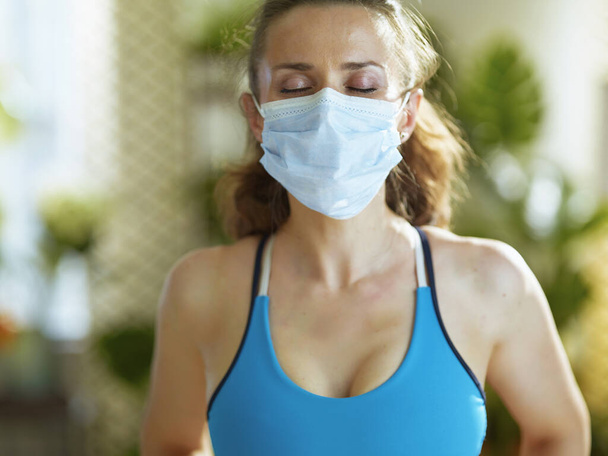 Life during coronavirus pandemic. fit middle age woman in sport clothes with medical mask catching breath after exercise. - Φωτογραφία, εικόνα