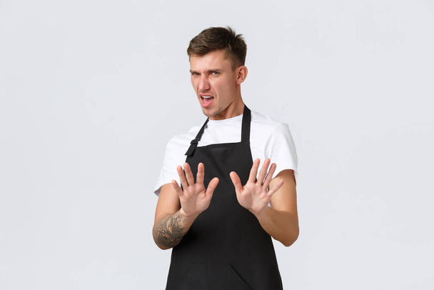 Employees, grocery stores and coffee shop concept. Displeased and reluctant picky guy step back and extend hands in stop sign, refusing and rejecting awful disgusting drink, white background - Photo, Image