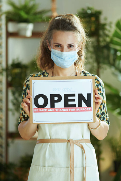 Opening small business after coronavirus pandemic. elegant small business owner woman in apron with medical mask showing open sign. - Fotografie, Obrázek