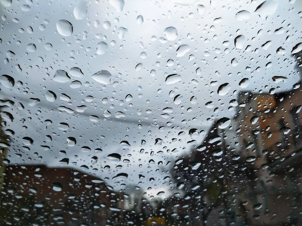 Calle de la ciudad vista a través de gotas de lluvia en el parabrisas del coche. Mal tiempo de otoño en el día lluvioso. Parabrisas del coche con gotas de lluvia en el parabrisas de cristal
. - Foto, Imagen