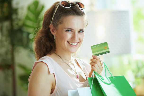 Portrait of smiling modern woman shopper in pink blouse with credit card and paper shopping bags. - Fotoğraf, Görsel