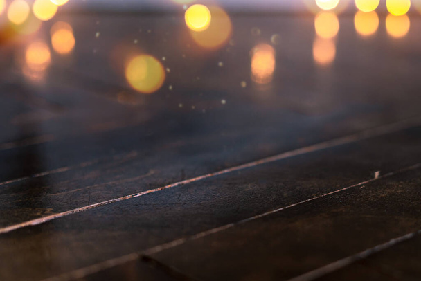  Pusty rustykalny drewniany stół z rozmytymi lampkami na tle. Jasny złoty bokeh kawiarni restauracji w ciemnym tle - Zdjęcie, obraz