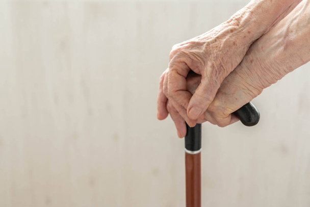 Idős kezek, boton nyugszanak. Közelről, ahogy egy öregasszony sétabotot tart. Női nyugdíjas kezei egy sétapálcán. Egy idős hölgy sétapálcával a kezében. A segítség fogalma idős korban - Fotó, kép