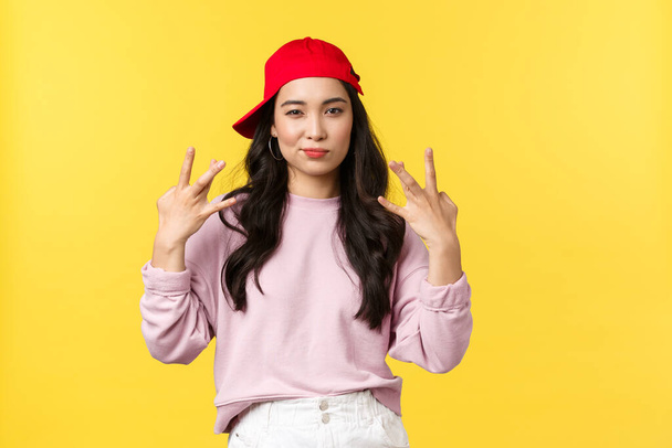 People emotions, lifestyle leisure and beauty concept. Stylish and cute hip-hop dancer girl, showing swag gesture and smirk sassy, acting confident and cool, standing yellow background - Foto, Imagem